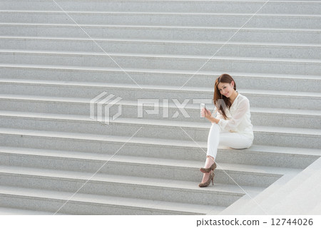 A woman sitting on the stairs and having a smartphone A woman sitting on the stairs and having a smartphone 12744026