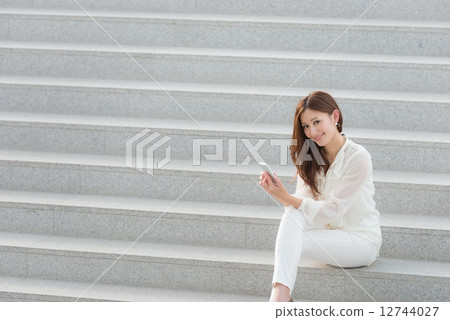 A woman sitting on the stairs and having a smartphone A woman sitting on the stairs and having a smartphone 12744027