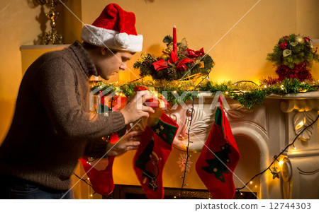 young father putting gifts in Christmas stockings at fireplace young father putting gifts in Christmas stockings at fireplace 12744303