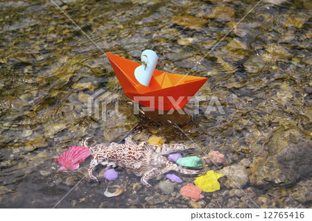 Orange paper boat floating in the water at the bottom of colorful seashells Orange paper boat floating in the water at the bottom of colorful seashells 12765416