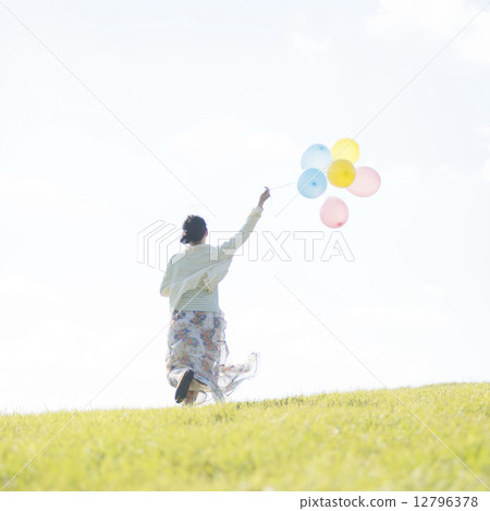 A rear view of a woman holding a balloon and running on the meadow A rear view of a woman holding a balloon and running on the meadow 12796378