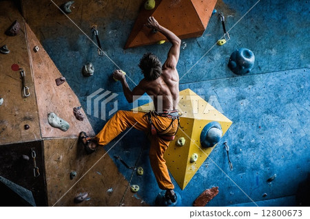 Muscular man practicing rock-climbing on a rock wall indoors 12800673