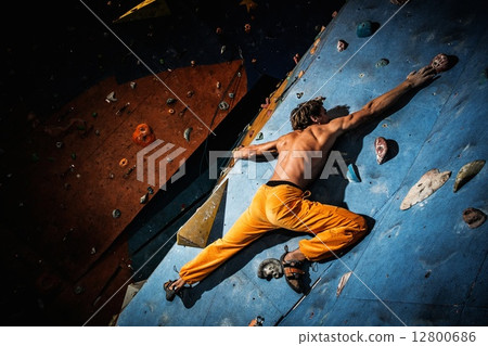 Muscular man practicing rock-climbing on a rock wall indoors 12800686