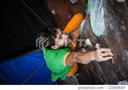 Muscular man practicing rock-climbing on a rock wall indoors 12800689