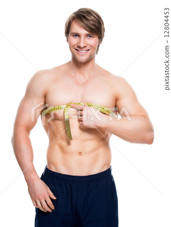 Young man with muscular torso uses measuring tape. 12804453