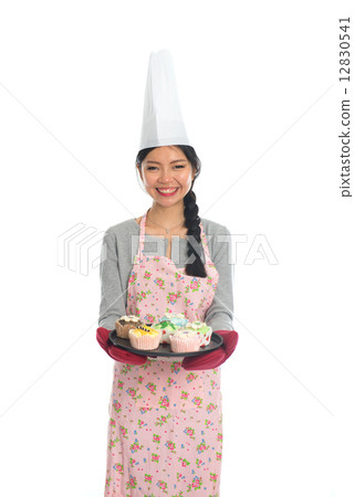 Young Asian girl baking bread and cupcakes, wearing apron and gl 12830541