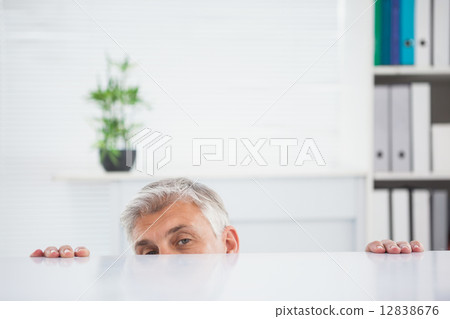 Nervous businessman peeking over desk 12838676