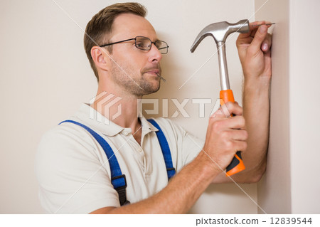 Handyman hammering nail in wall Handyman hammering nail in wall 12839544