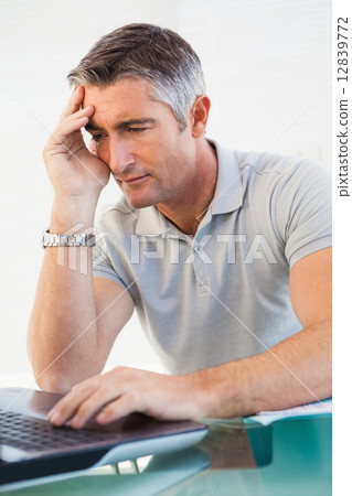 Tired man sitting and using his laptop 12839772