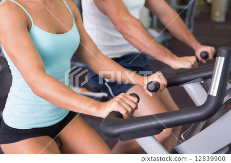Mid section of couple working on exercise bikes at gym 12839900