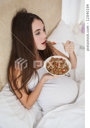 Pregnant brunette eating cereal in bed 12840194