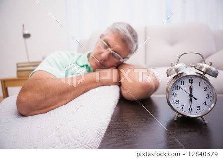 Man dozing on the couch beside alarm clock Man dozing on the couch beside alarm clock 12840379