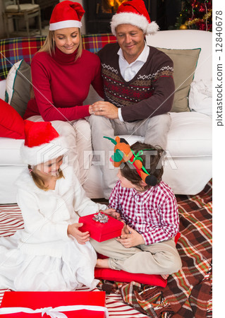 Parents sitting on couch looking children opening their gifts 12840678