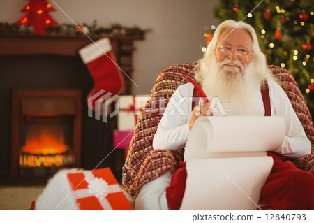 Smiling santa writing list on the armchair 12840793