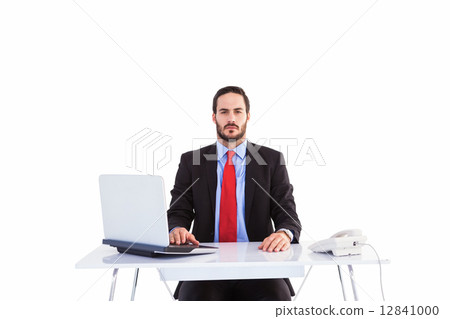 Unsmiling businessman sitting at desk Unsmiling businessman sitting at desk 12841000
