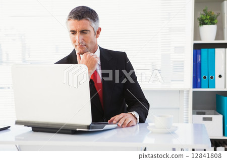 Focused businessman in suit using his laptop 12841808