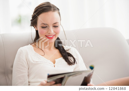 Pretty brunette reading magazine on the couch 12841868