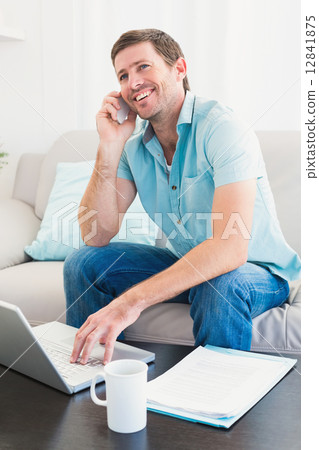 Smiling man on a phone with a laptop at home 12841875