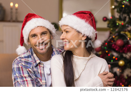 Festive couple in santa hat hugging on the couch Festive couple in santa hat hugging on the couch 12842576