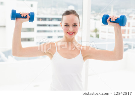 Fit brunette holding blue dumbbells 12842817