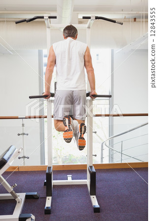 Fit man doing pull ups in fitness studio 12843555