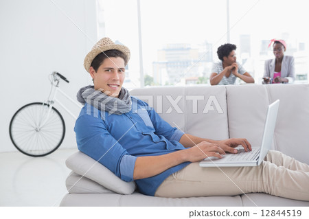 Young creative man using laptop on couch Young creative man using laptop on couch 12844519