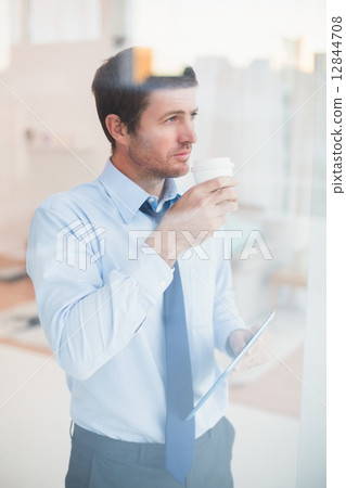 Businessman holding disposable cup and tablet looking out the wi 12844708