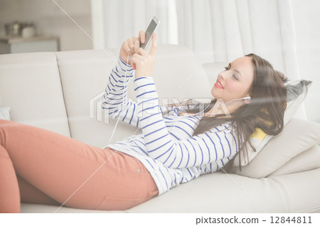 Pretty brunette listening to music on the couch Pretty brunette listening to music on the couch 12844811