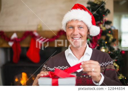Smiling handsome man in santa hat opening a gift 12844834