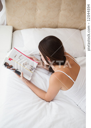 Pretty brunette reading magazine on bed Pretty brunette reading magazine on bed 12844894
