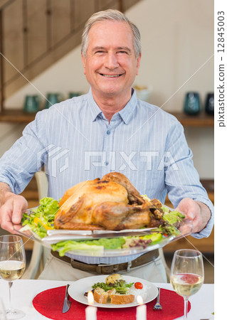 Happy mature man holding roast turkey at christmas dinner 12845003