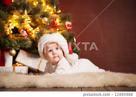 Happy baby wearing Santa hat over christmas tree Happy baby wearing Santa hat over christmas tree 12893988