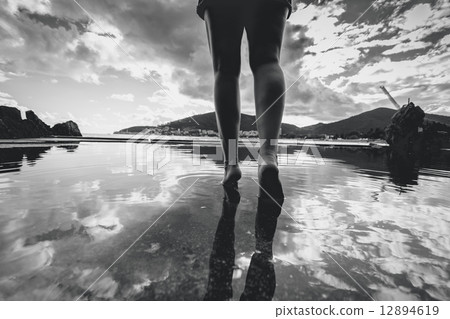 Monochrome photo of female legs walking on water with sky reflec 12894619