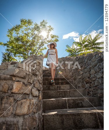 woman in white hat walking down the stone stairs at sunny day 12894779