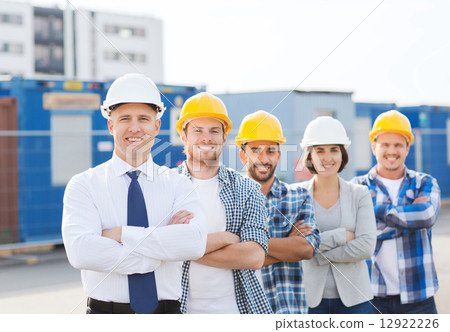 group of smiling builders in hardhats outdoors group of smiling builders in hardhats outdoors 12922226