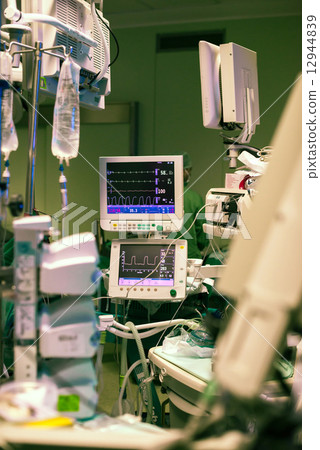 Heart rate monitors in surgery room with iv solution infusion on the foreground and green lights ope 12944839