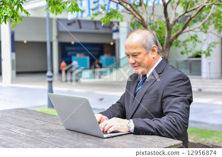 Senior Asian businessman connecting to his business using mobile device at outdoor Senior Asian businessman connecting to his business using mobile device at outdoor 12956874