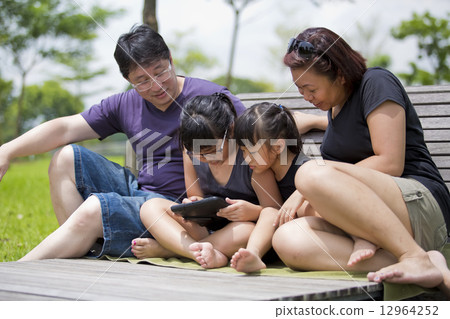 Young Asian family bonding in park playing tablet Young Asian family bonding in park playing tablet 12964252