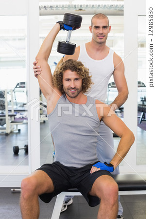 Trainer assisting young man with dumbbell in gym Trainer assisting young man with dumbbell in gym 12985830