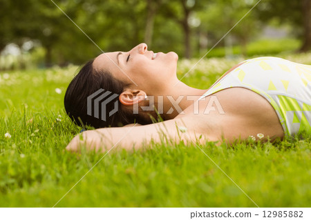 Peaceful fit brunette lying on the grass Peaceful fit brunette lying on the grass 12985882