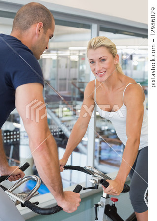 Smiling fit couple working on exercise bikes at gym 12986029