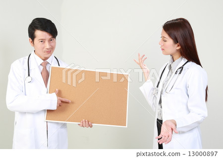 Male doctor holding pointing at signboard and female doctor looking with wonder 13000897