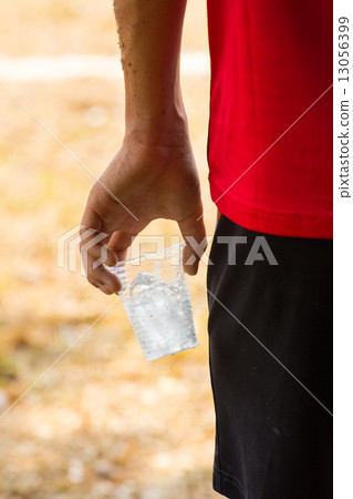 hand of athlete holding glass of iced water against strong sunli 13056399