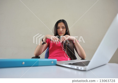A young and beautiful Asian female student pondering / brainstorming at her desk in front of laptop A young and beautiful Asian female student pondering / brainstorming at her desk in front of laptop 13063728