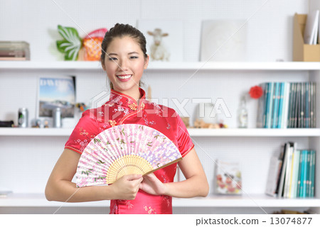 Young chinese in Cheongsam with Chinese Fan in front of bookshelf 13074877