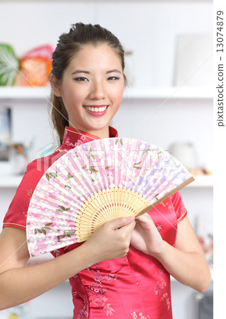 Young chinese in Cheongsam with Chinese Fan in front of bookshelf 13074879