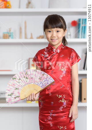 Little Chinese girl in Cheongsam with Chinese Fan in front of bookshelf 13074911