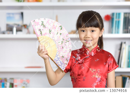Little Chinese girl in Cheongsam with Chinese Fan in front of bookshelf 13074916