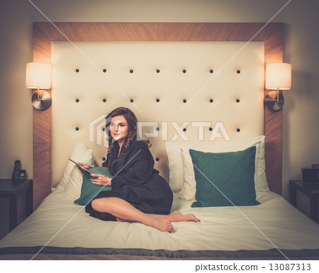 Woman in bathrobe lying on a bed with tablet pc Woman in bathrobe lying on a bed with tablet pc 13087313