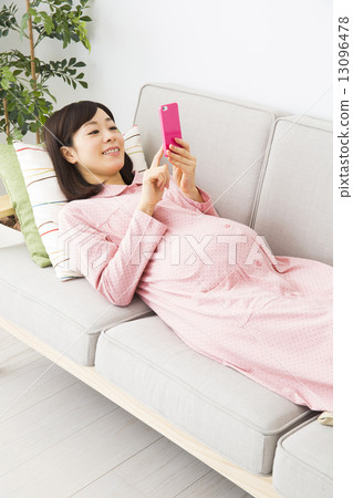 Pregnant woman operating a smartphone on the sofa 13096478